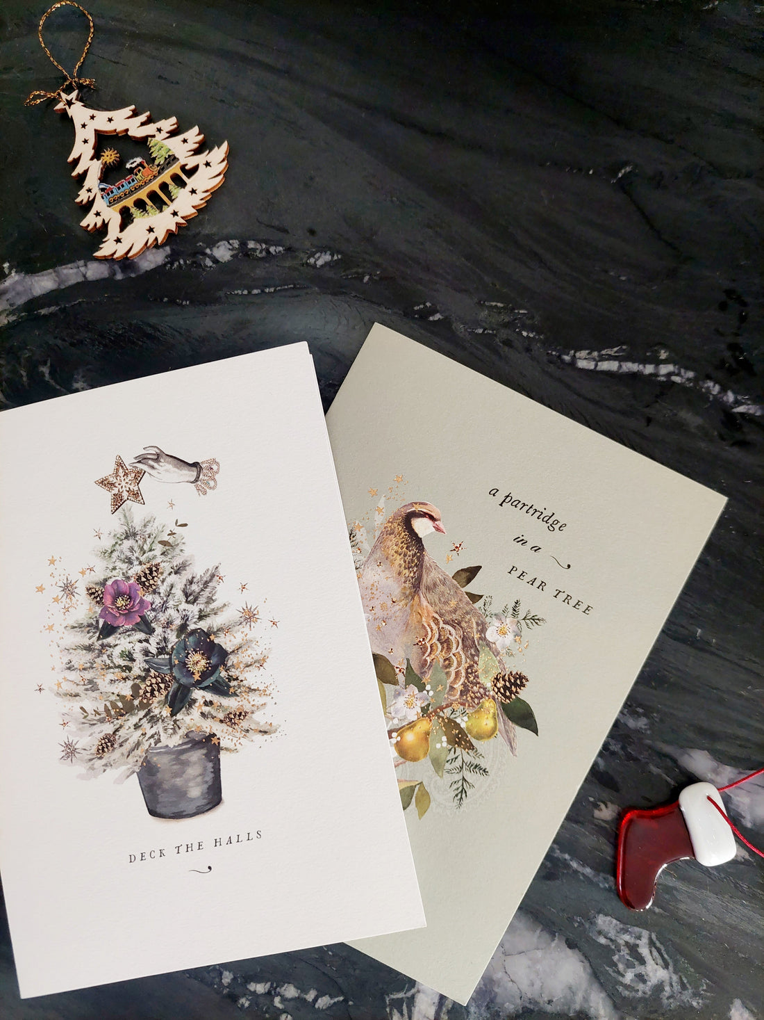 Two Christmas greeting cards on a black marble background with decorative Christmas ornaments.