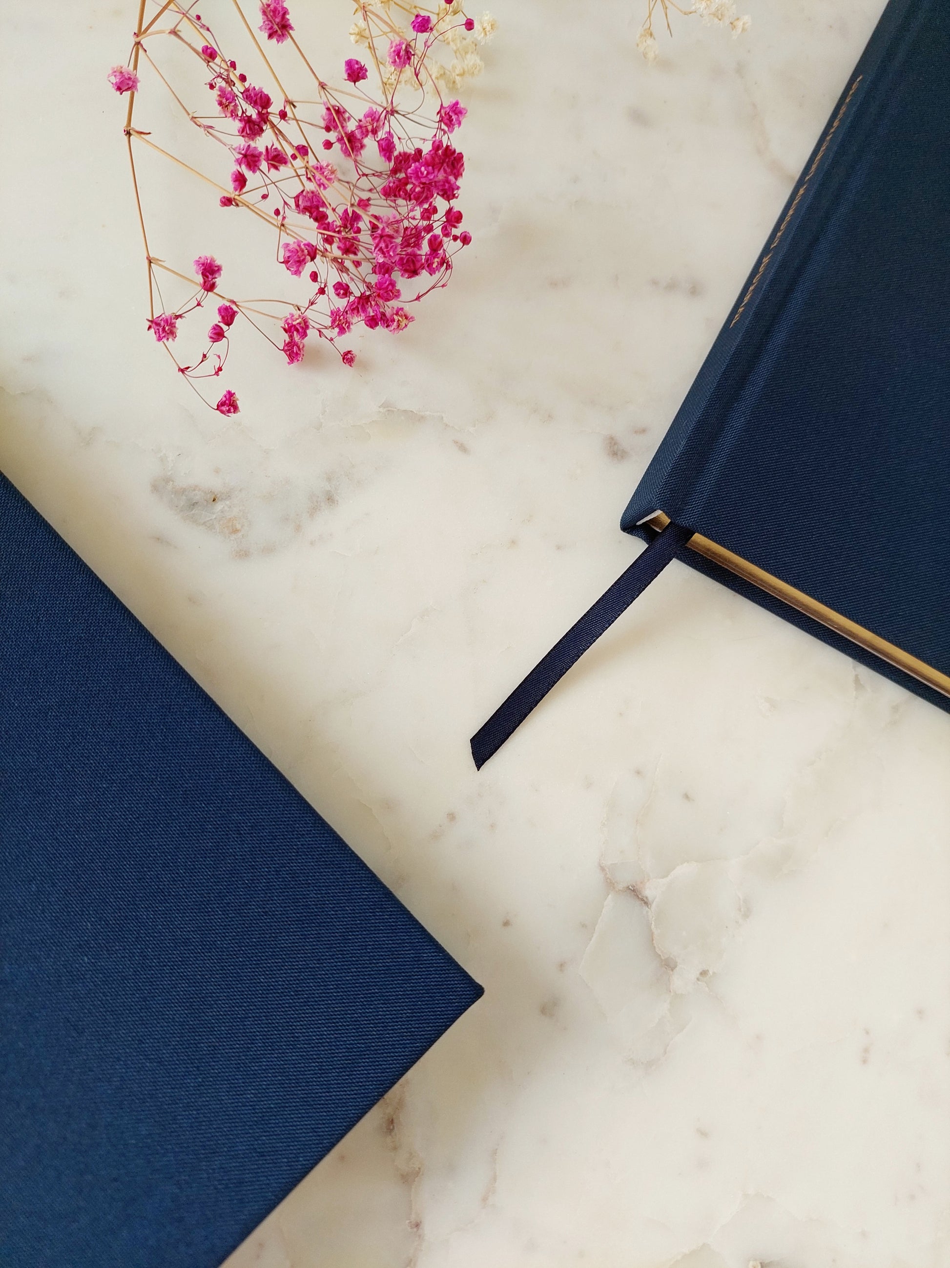 Two blue books on a marble surface with pink flowers.